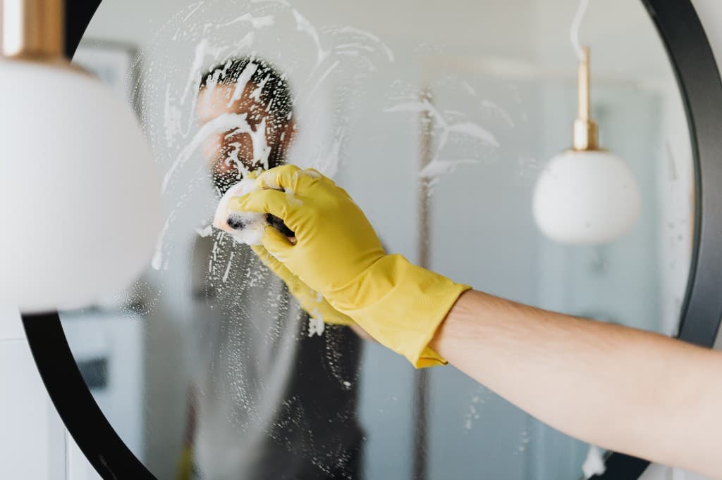Detailed bathroom mirror cleaning with professional supplies and soap suds